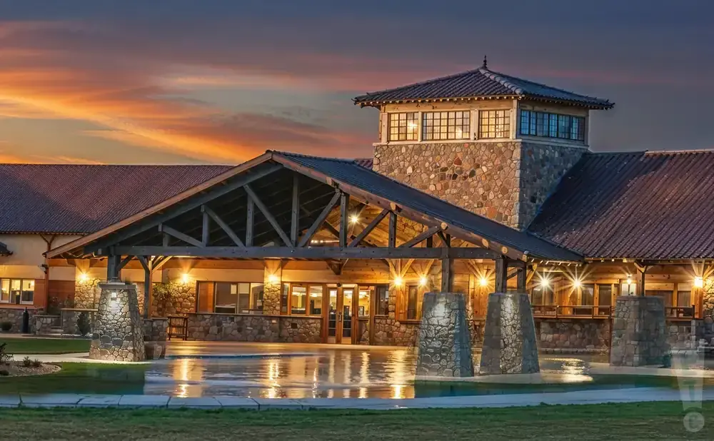 A grand entrance to a lodge with a stone tower and wooden beams is lit up at dusk.