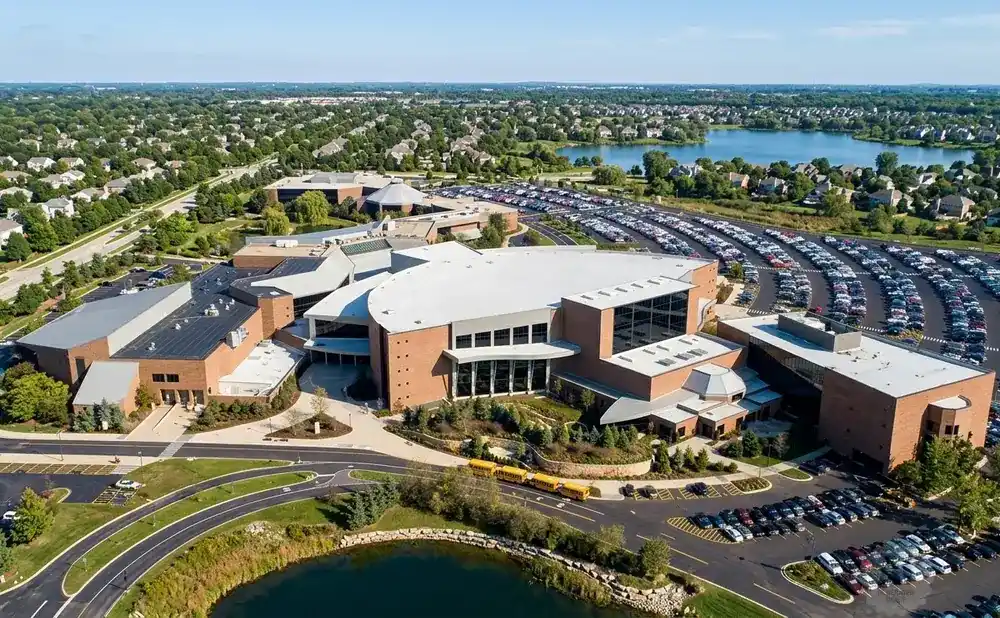 Aerial view of a large church complex with a sprawling parking lot, a pond, and a lake in the background.