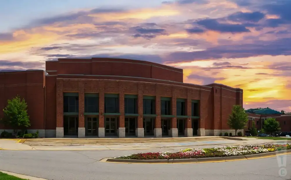 A brick building with large windows and a curved facade, set against a dramatic sunset sky.