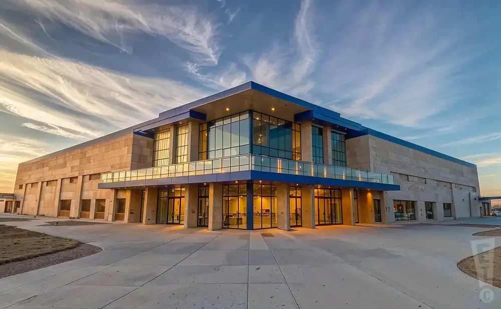 Modern tan and blue building with large glass windows under a dramatic sky.