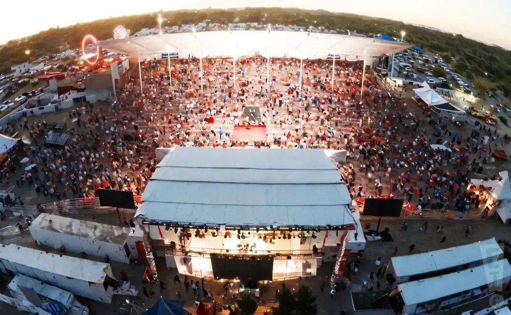 An aerial view of a crowded outdoor concert with a stage and seating area.