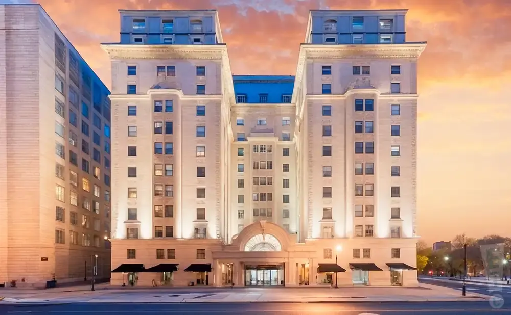 A grand, illuminated hotel with two towers stands tall against a dramatic sunset sky.