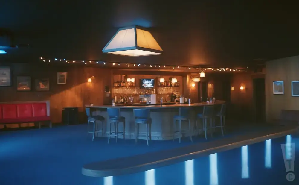 A dimly lit bar with a long counter, stools, and a red booth.