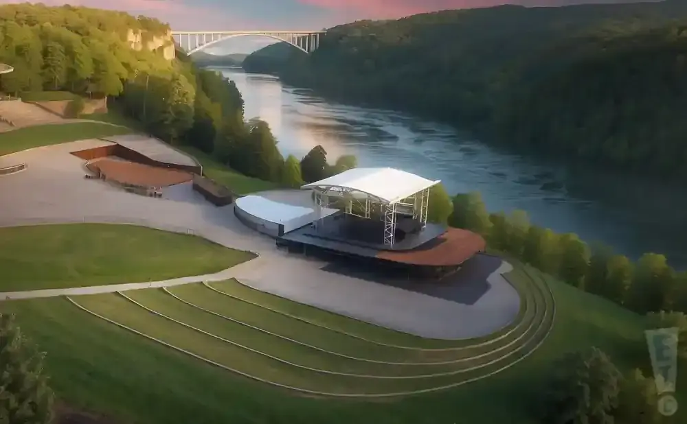 Outdoor amphitheater stage overlooking a wide river with a bridge in the distance.