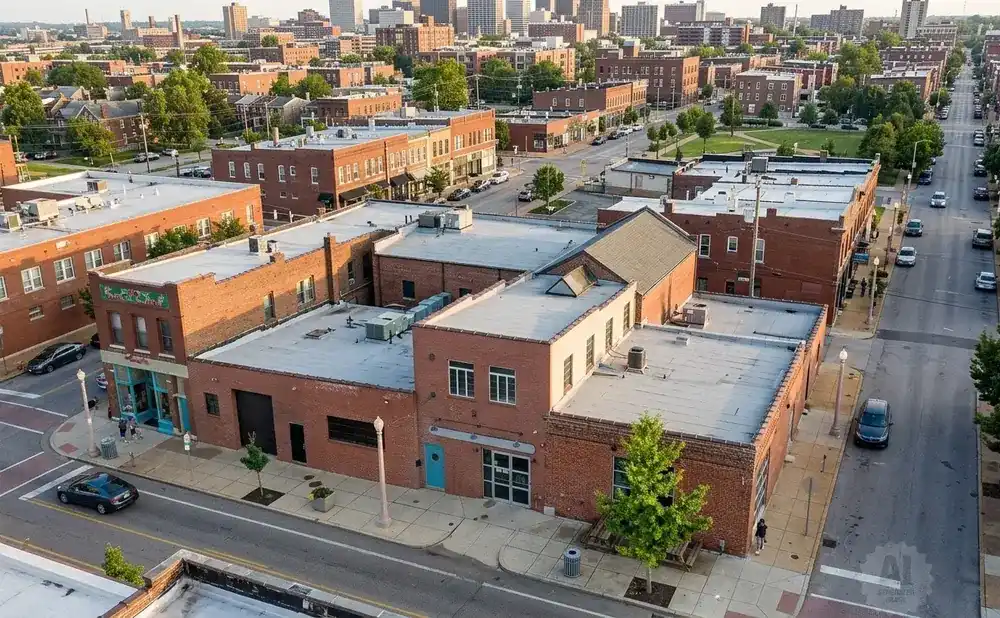 Aerial view of a city street with brick buildings, trees, and cars.