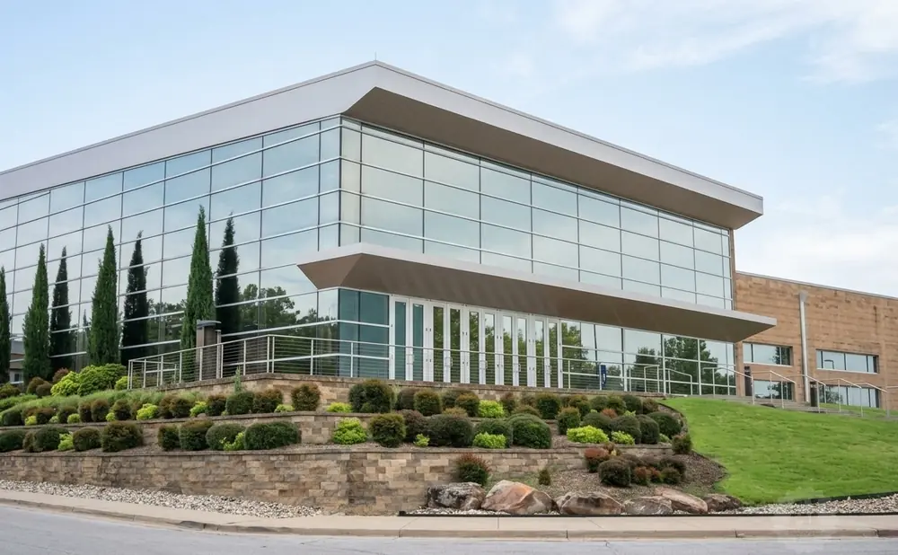 Modern glass building with landscaped terraces and trees under a cloudy sky.