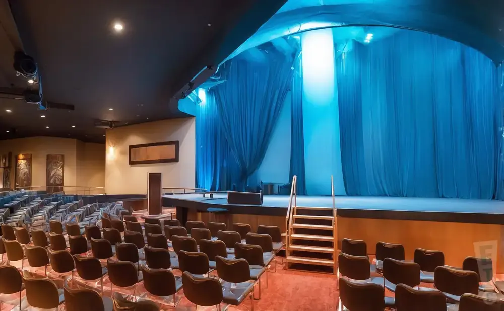 An empty theater with blue curtains on stage and rows of seats.