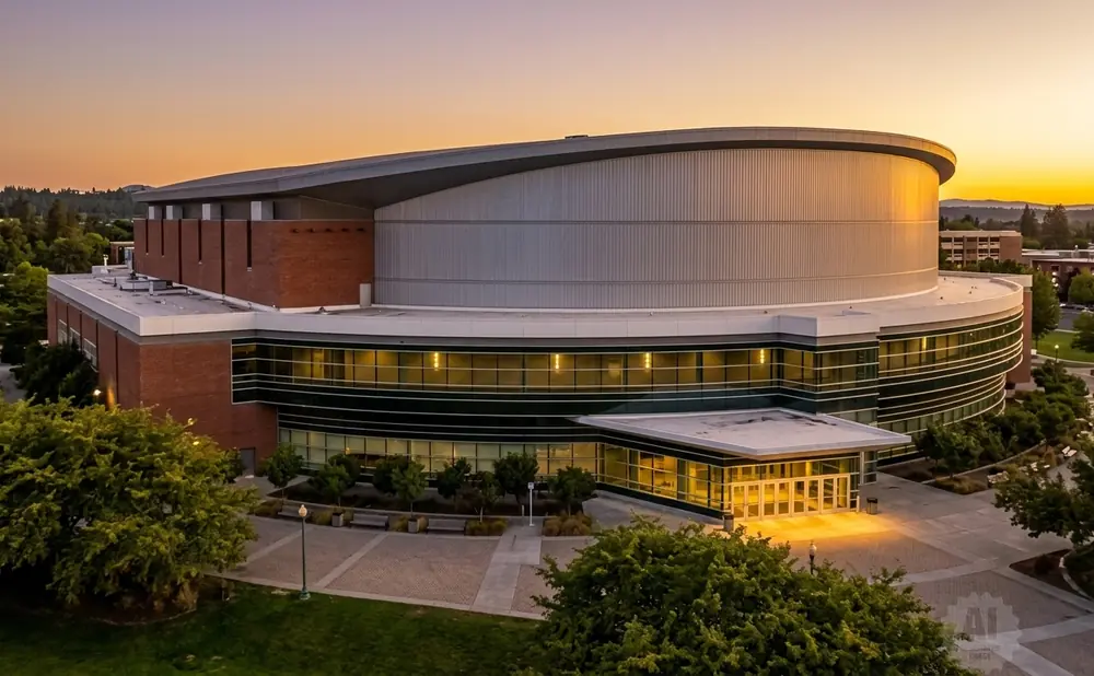 Modern brick and glass arena with a curved metal roof at sunset.