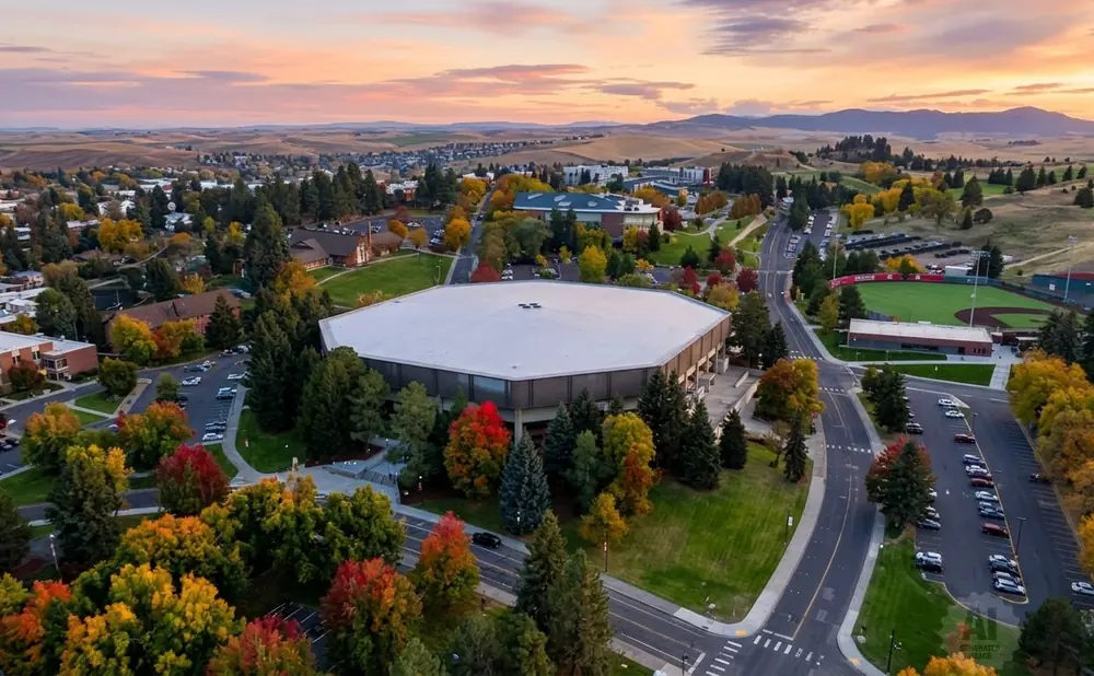 Aerial view of a university campus with colorful fall foliage, an arena, and a baseball field at sunset.
