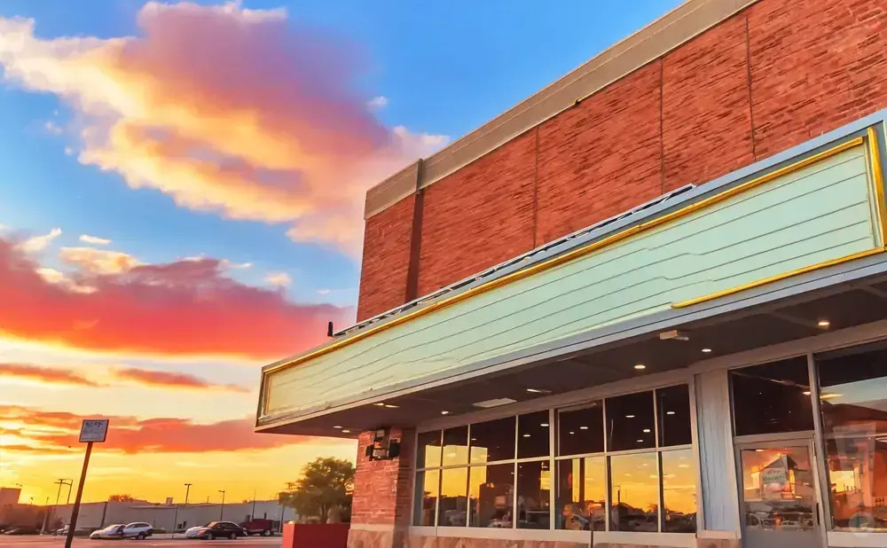 A storefront with a blank marquee under a colorful sunset sky.