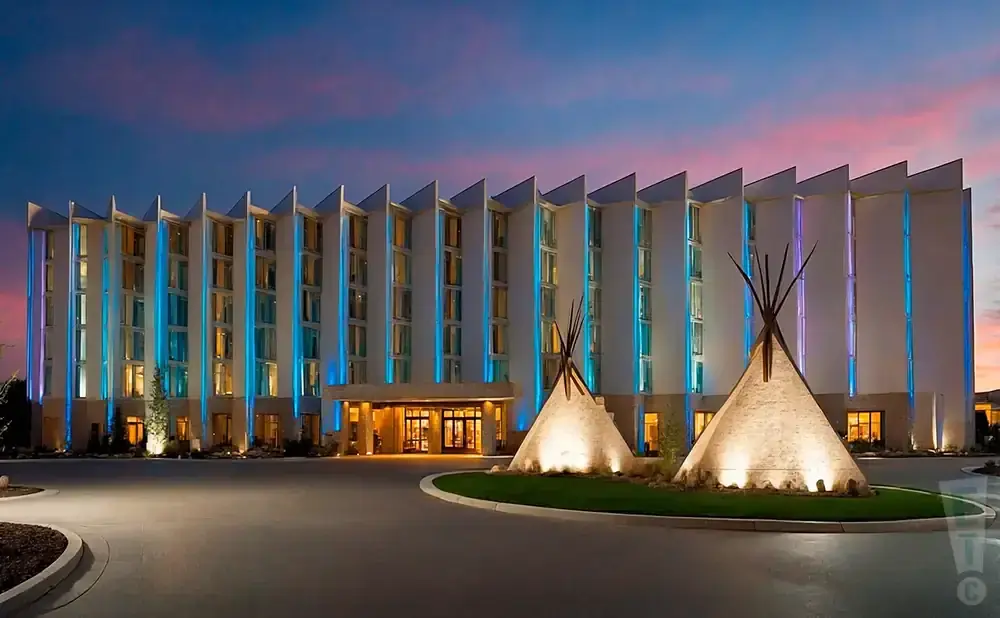 Hotel lit with blue lights at dusk, with two teepees in front.