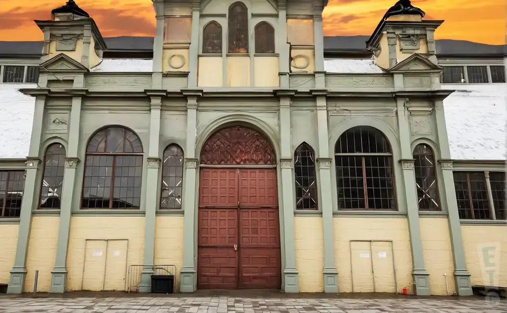 An ornate, weathered building with large windows and double doors under a dramatic orange sky.