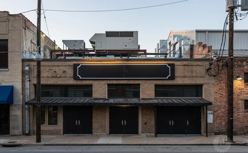 Exterior of a brick building with a black banner and awnings over dark doors.