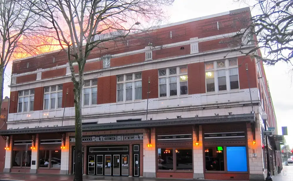 Red brick building with large windows and a dark awning over the storefronts.