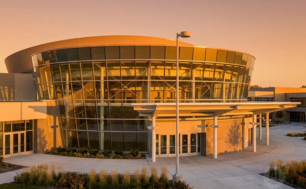 Modern glass-fronted building with curved architecture illuminated by sunset.