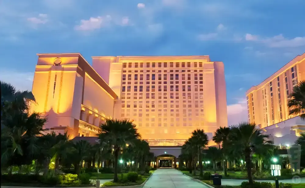 A grand hotel at twilight, illuminated with warm lights, with palm trees in the foreground.