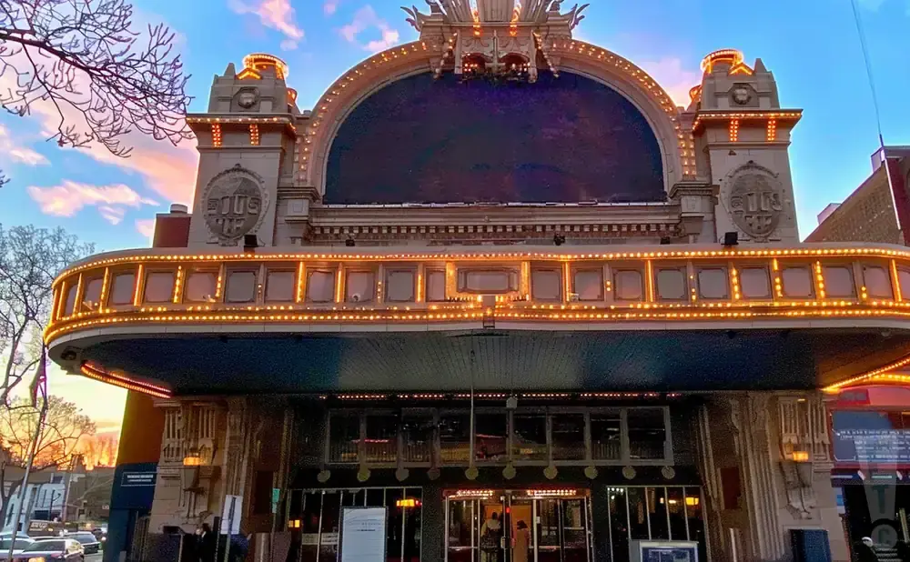 Grand theater facade with arched marquee lit by marquee lights at sunset.