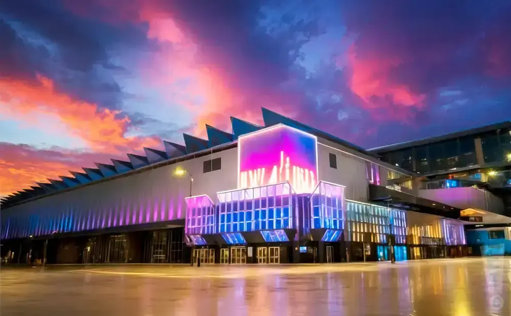 A modern building illuminated with vibrant pink and blue lights under a dramatic sunset sky.