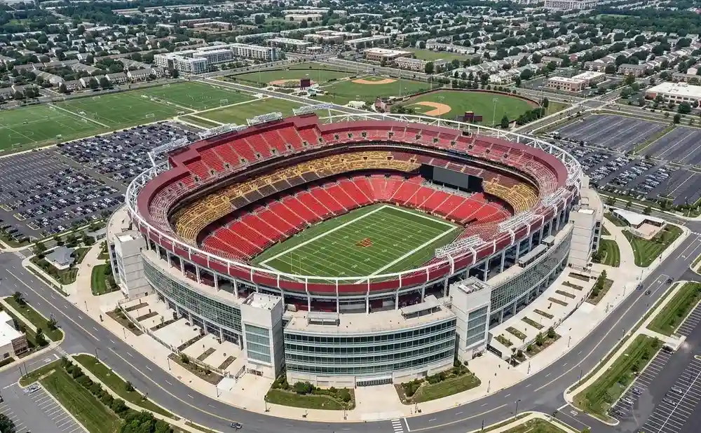 Aerial view of a large, red-seated football stadium surrounded by parking lots and residential areas.