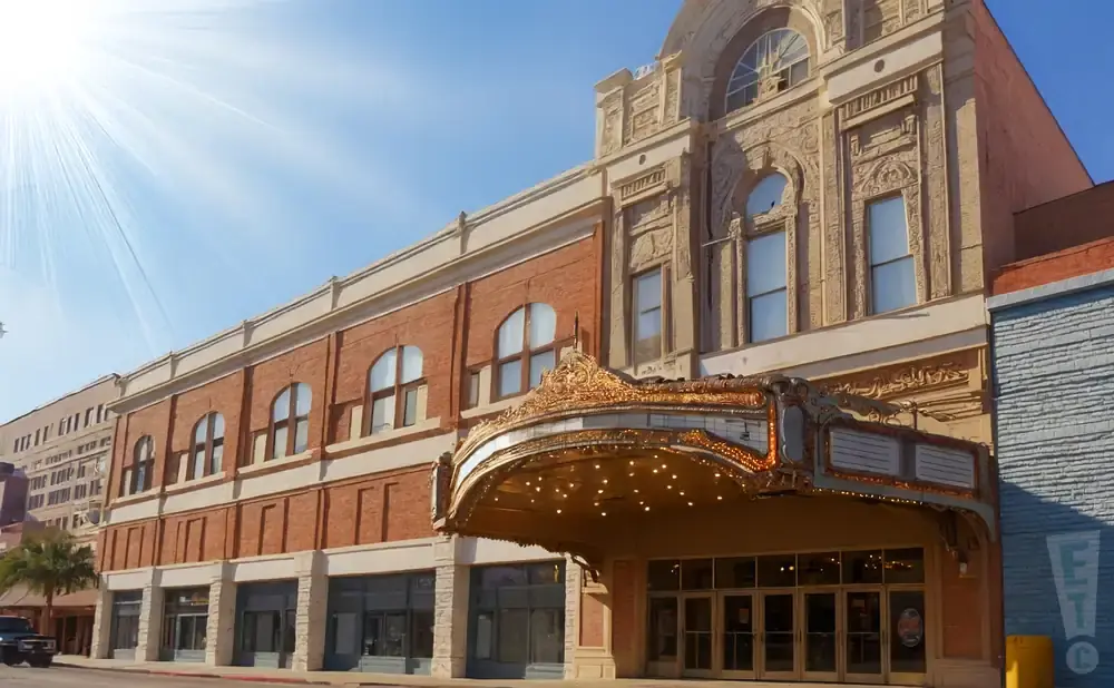 A historic theater with ornate marquee and brick facade under a bright, sunny sky.