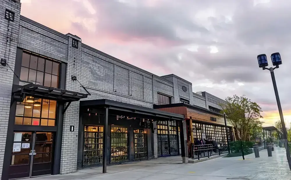 Modern brick building with large glass garage doors and outdoor seating under a cloudy sky.