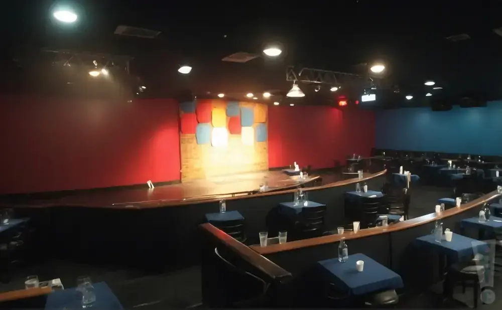 A comedy club stage with red and blue walls, and tables set up in the audience area.
