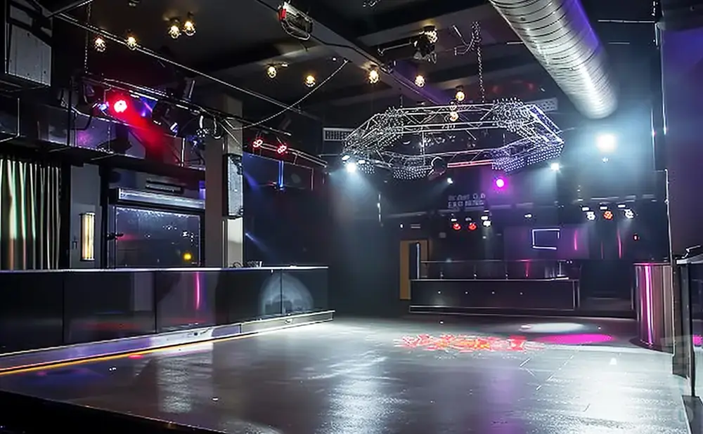 An empty, modern nightclub with a dance floor, bar, and stage lighting.