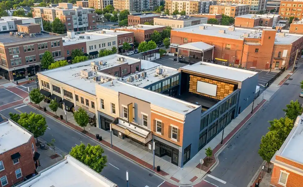 Aerial view of a modern theatre building with a large screen and an outdoor stage, surrounded by brick buildings and trees.