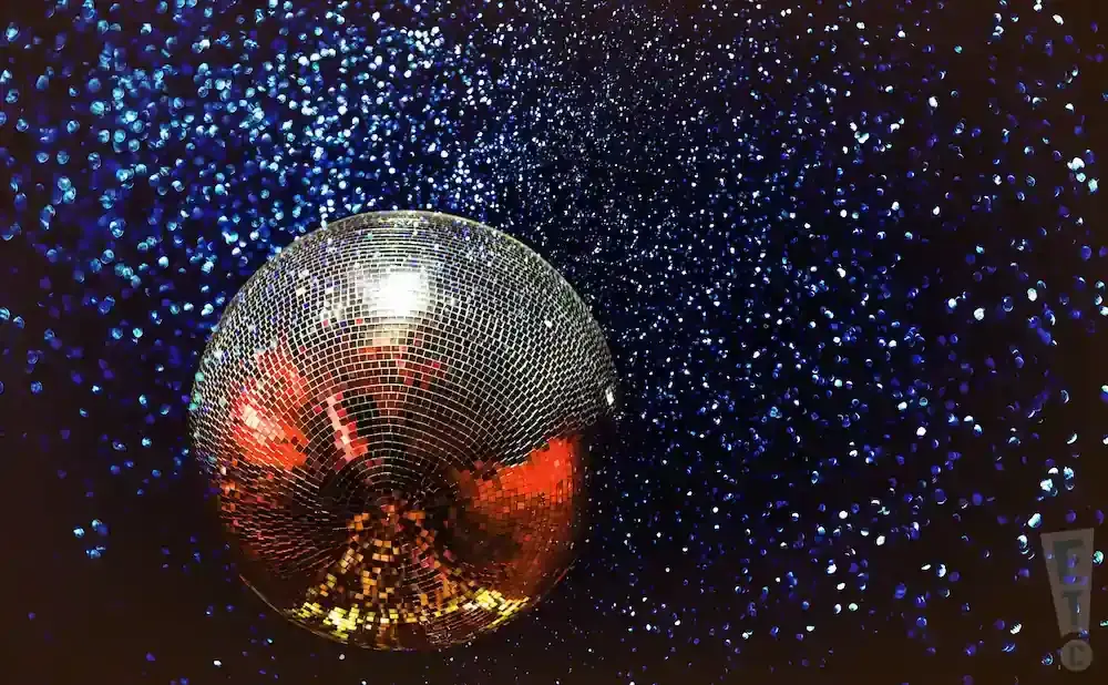 A disco ball sparkles against a dark background filled with blue glitter.