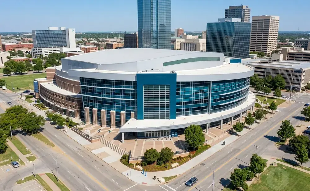 Aerial view of a large, modern arena with a curved glass exterior, surrounded by city buildings and trees.