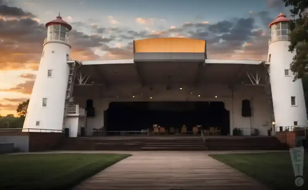 Outdoor amphitheater with two lighthouse-like towers, stage, and wooden walkway at sunset.