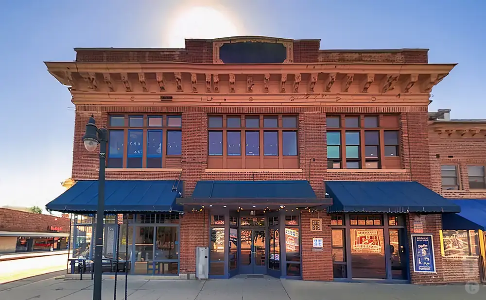 Exterior of a two-story brick building with large windows, blue awnings, and a decorative cornice.