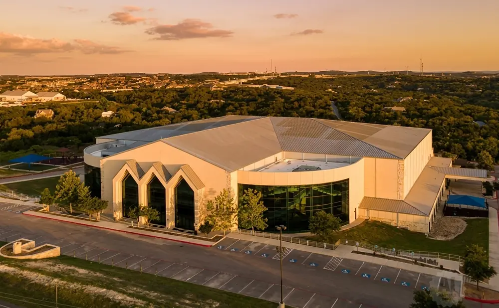 Aerial view of a large modern building with a silver roof and tan exterior walls during sunset.