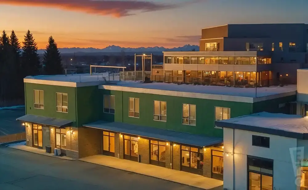 Modern building with green exterior and large windows at sunset, with mountains in the background.