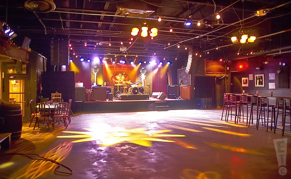 Empty concert hall with stage, drum set, and bar seating.