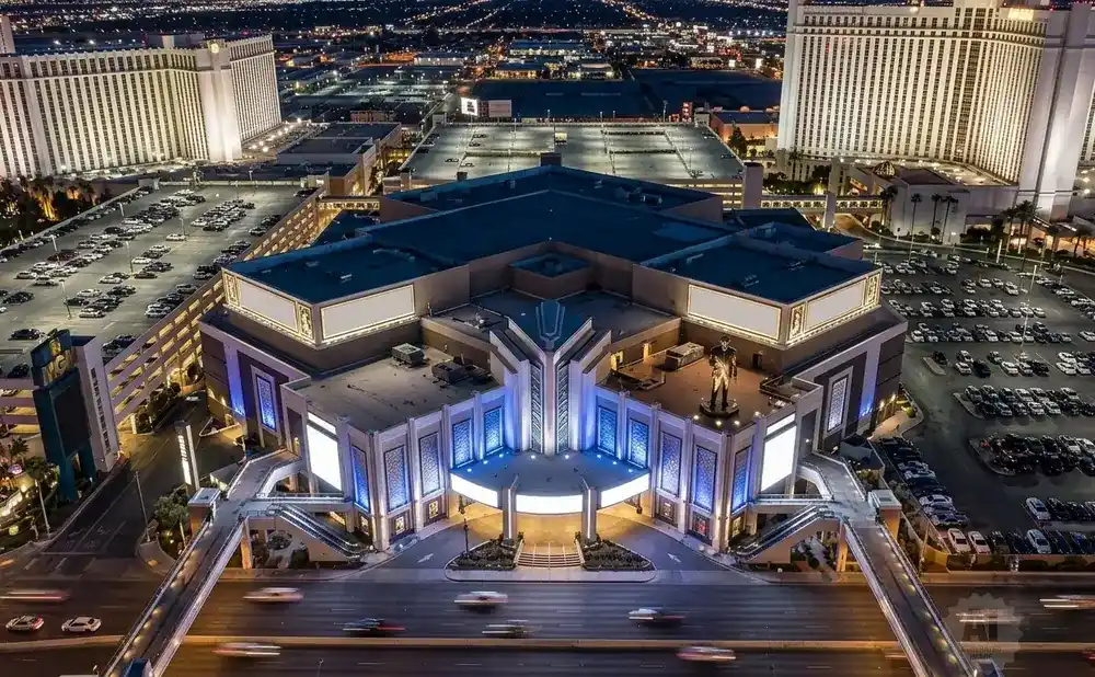 Aerial view of a large hotel and casino complex at night, with a parking lot filled with cars and a statue of Elvis Presley.