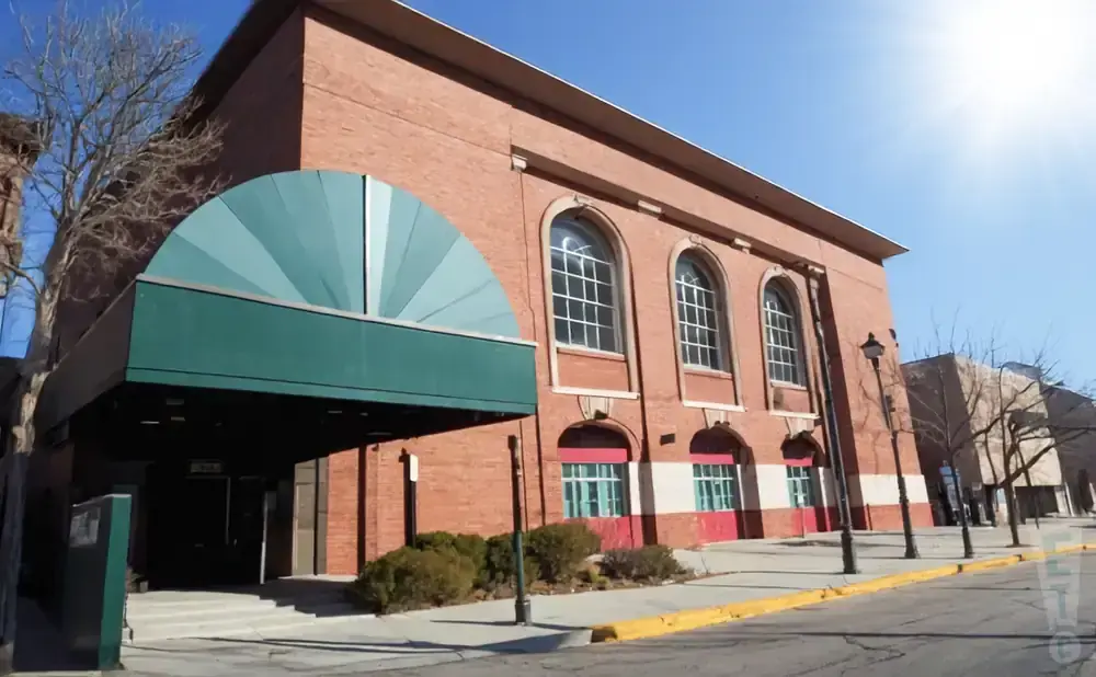 A brick building with arched windows and a green awning entrance on a sunny day.