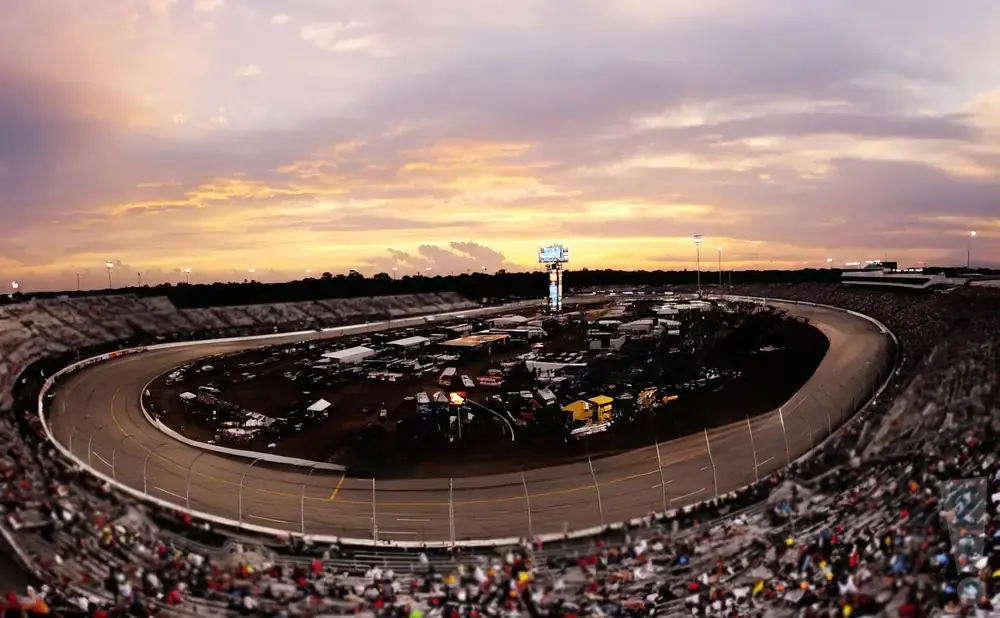 A panoramic view of a race track at sunset with spectators in the stands.