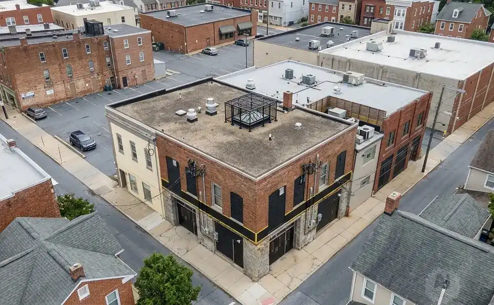 Aerial view of a brick building with black shutters and doors, a flat roof with a metal cage, and yellow trim.
