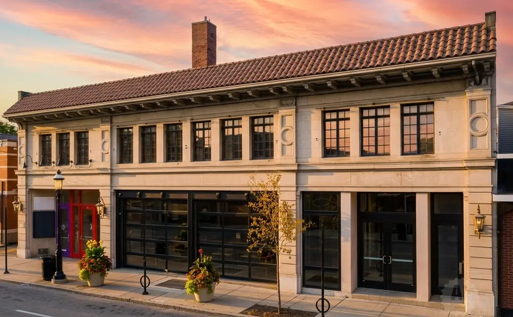 Exterior of a historic building with a tiled roof, large windows, and a brick chimney, at sunset.