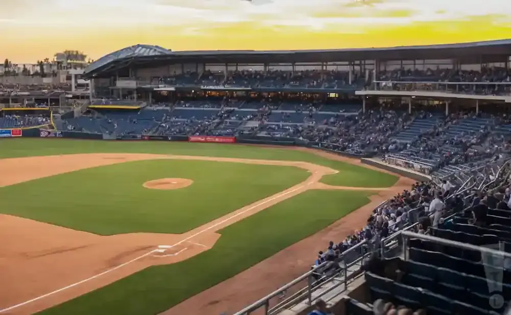 A baseball stadium with seats filled with spectators during a sunset game.