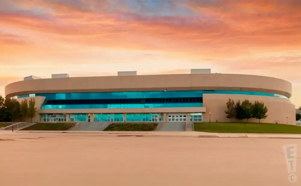Modern curved building with blue windows under a colorful sunset sky.