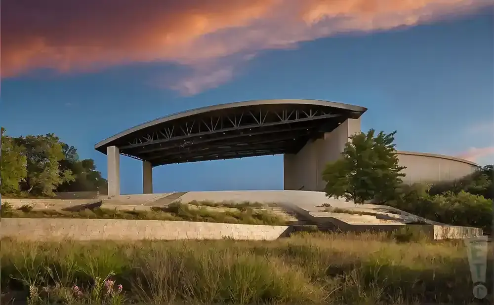 An outdoor amphitheater with a curved roof stands against a blue sky with orange clouds.