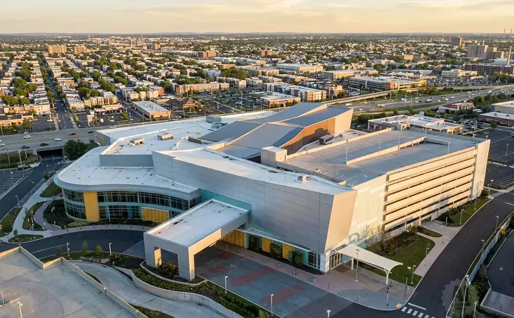 Aerial view of a modern complex with a large, multi-story building and surrounding urban landscape at sunset.
