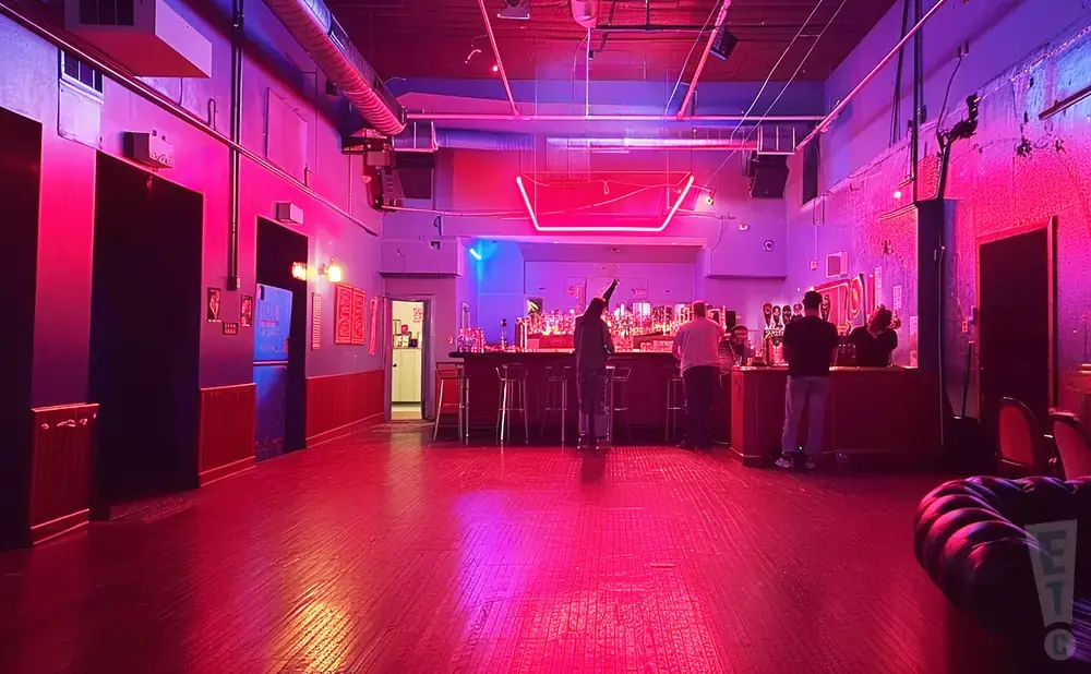 Interior of a bar with neon lights, a bar, and people.