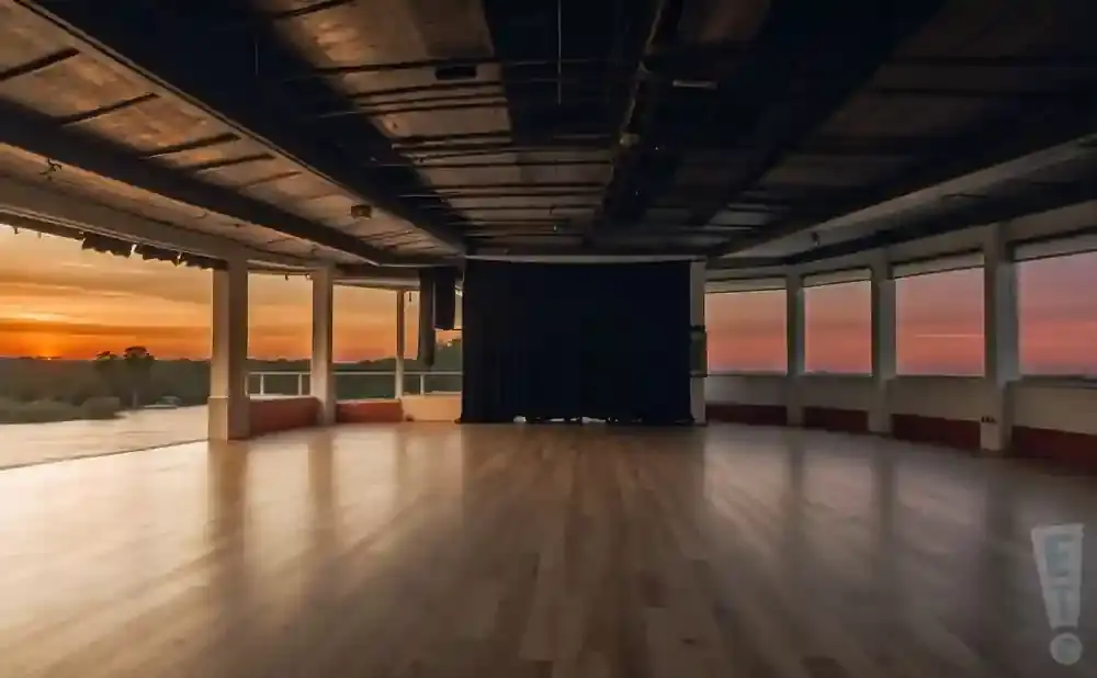 An empty studio with large windows overlooking a sunset, a projector screen, and a wooden floor.