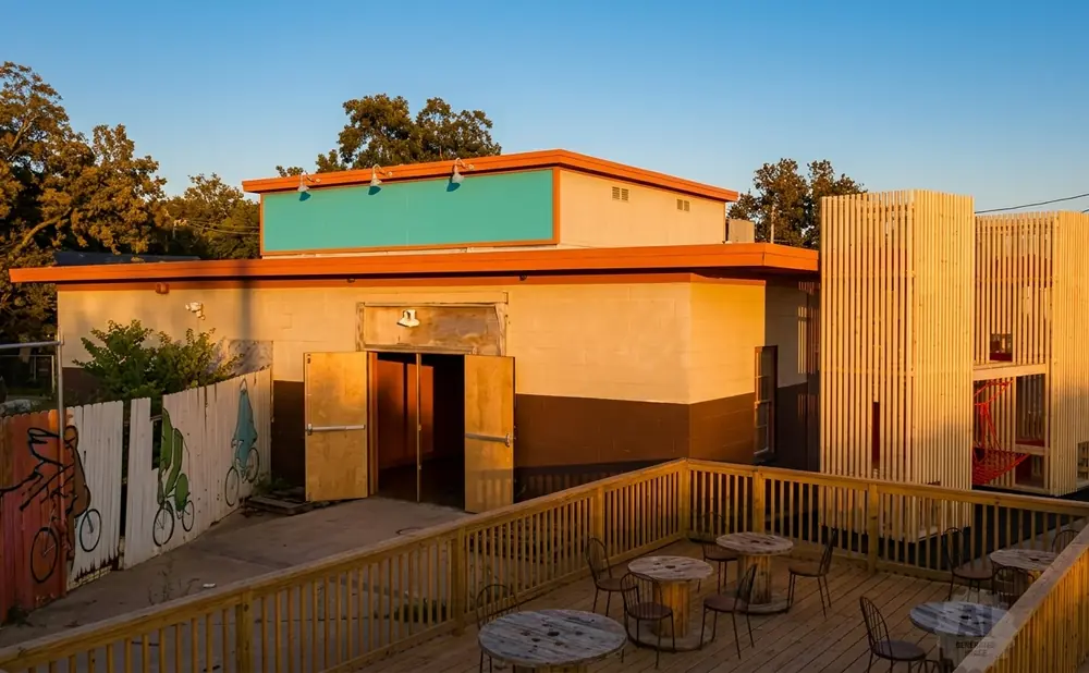 A building with a bright teal sign, orange trim, and a wooden deck with tables and chairs.