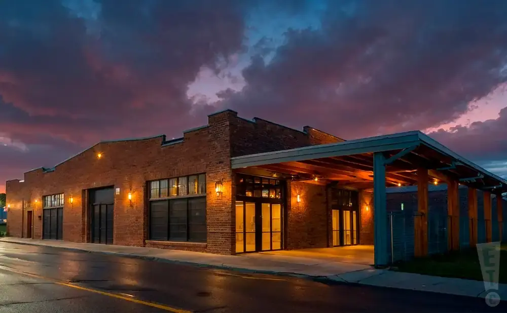 Exterior of a brick building with large windows and a covered entryway at dusk.
