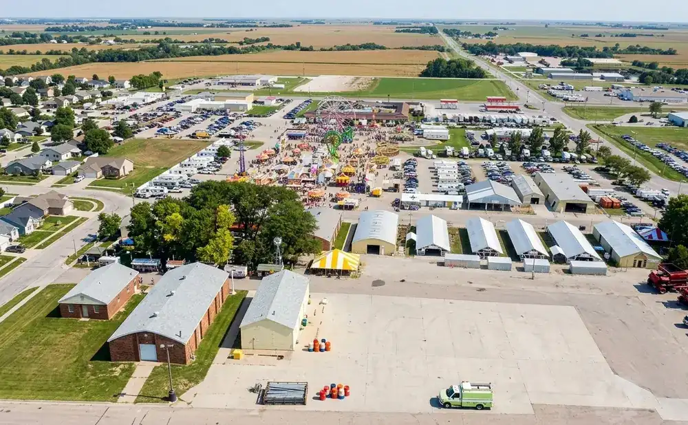 Aerial view of a fairgrounds with rides, games, buildings, and surrounding residential and agricultural areas.