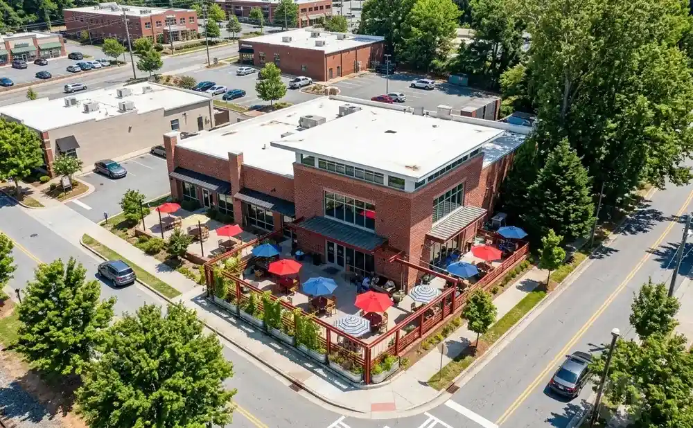 An aerial view of a brick building with an outdoor patio filled with tables and umbrellas.